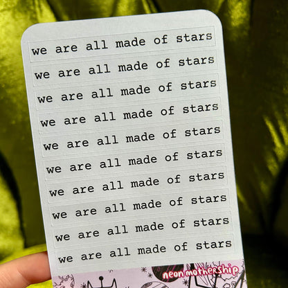 Sticker sheet with 'we are all made of stars' text held by a hand against a green background