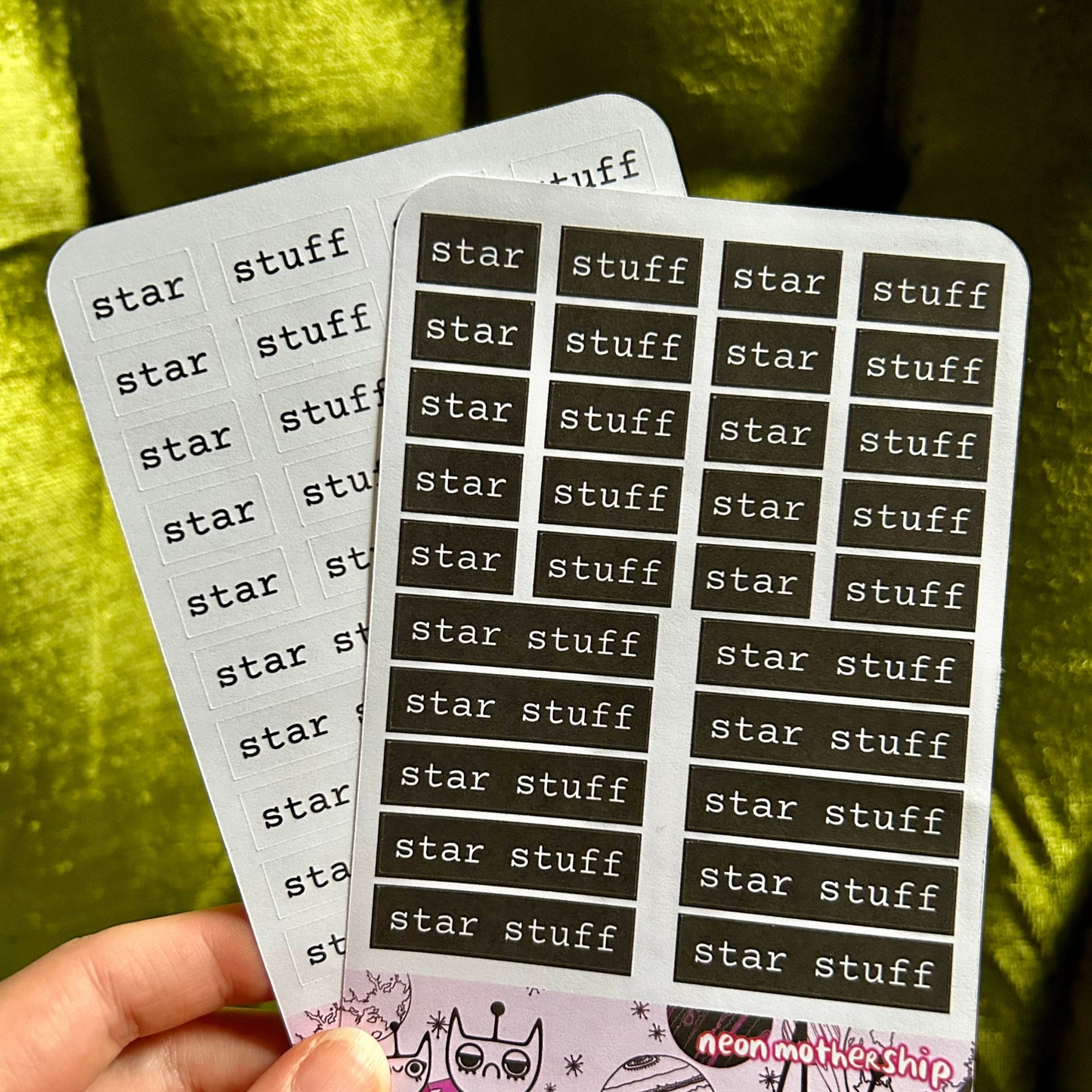 Two sticker sheets with 'star stuff' text held by a hand against a green fabric background