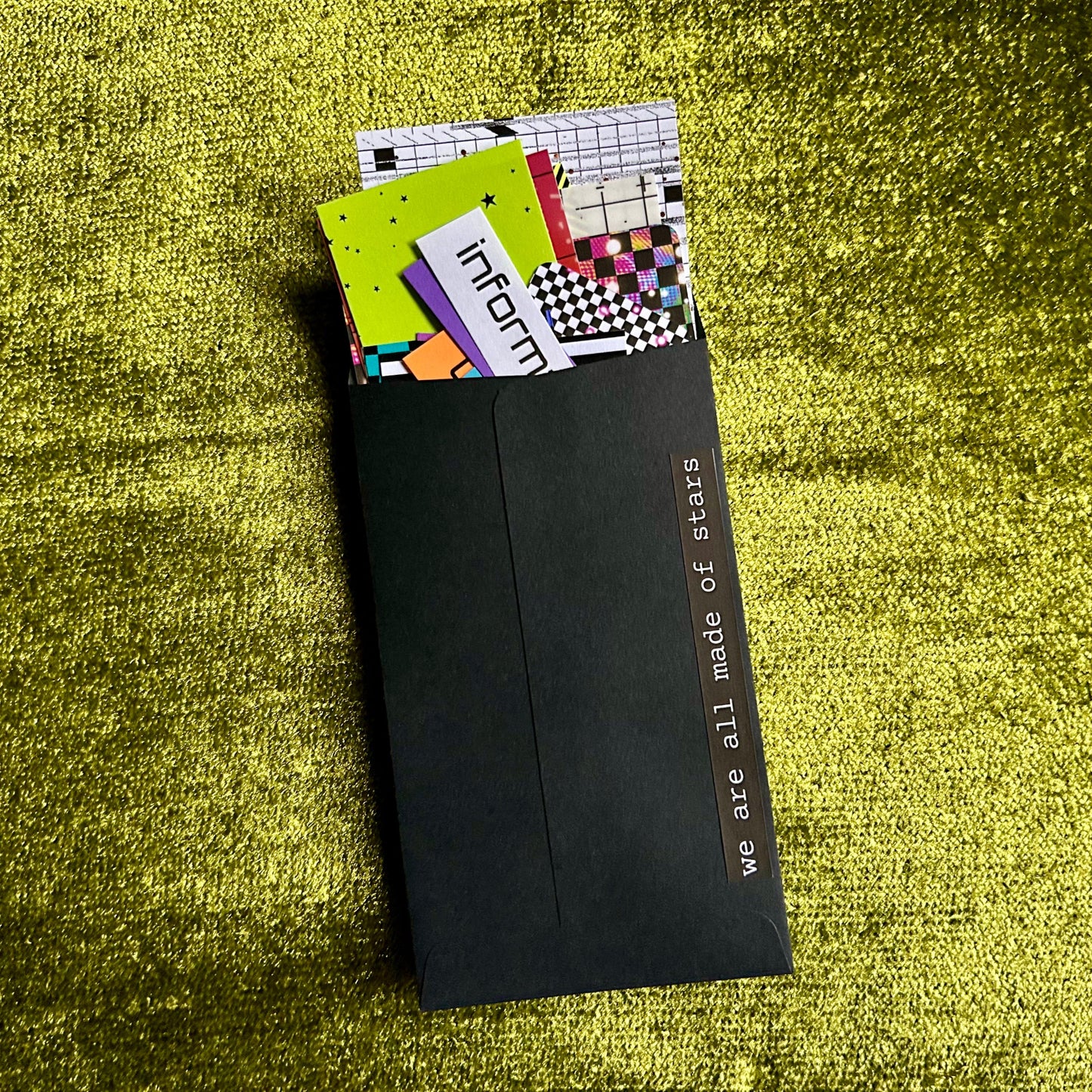 Black envelope with colorful papers on a green textured surface