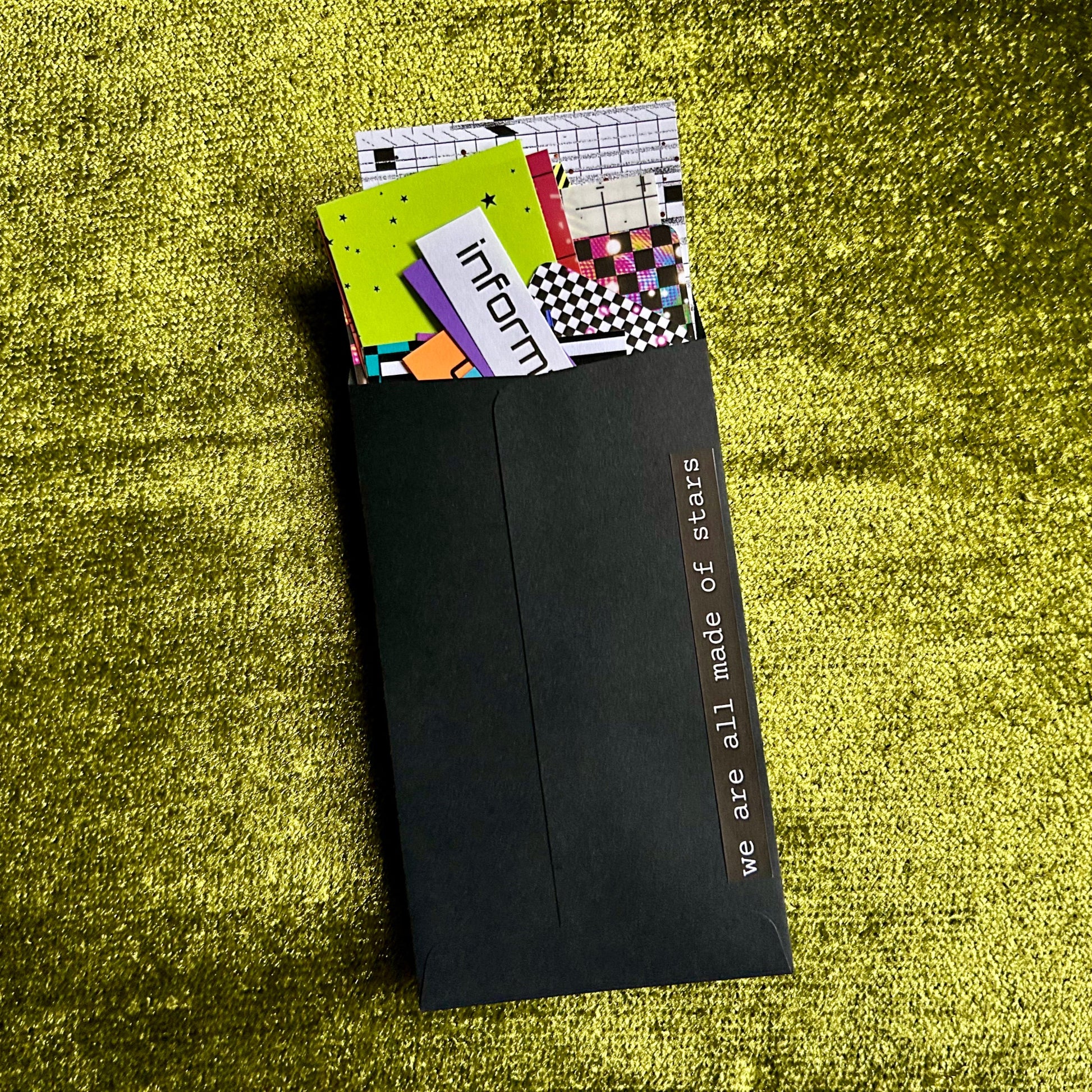 Black envelope with colorful papers on a green textured surface