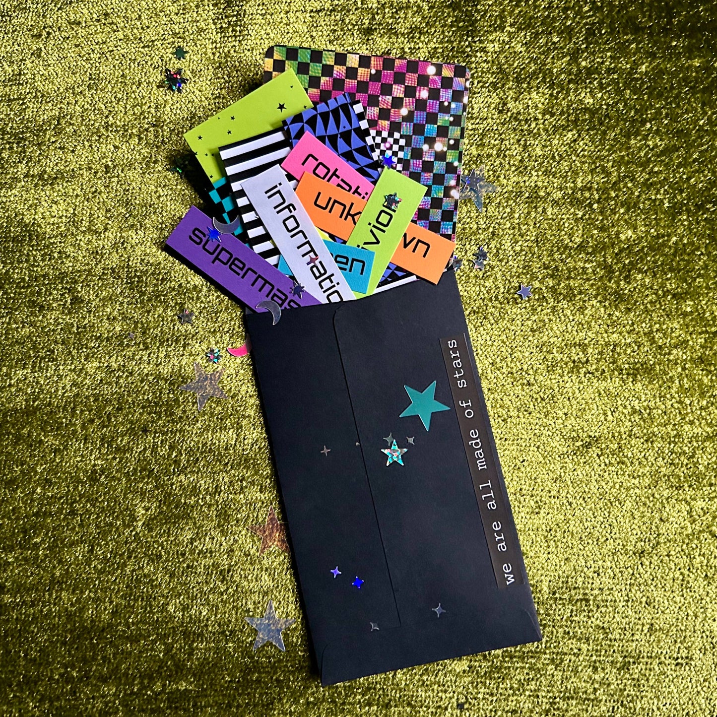 Colorful papers with various designs and text on a textured green surface.