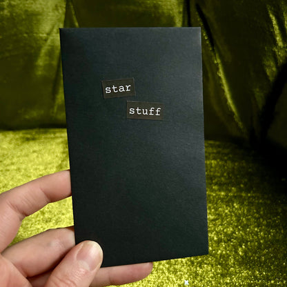 Black envelope with 'star stuff' title held by a hand against a green glittery background