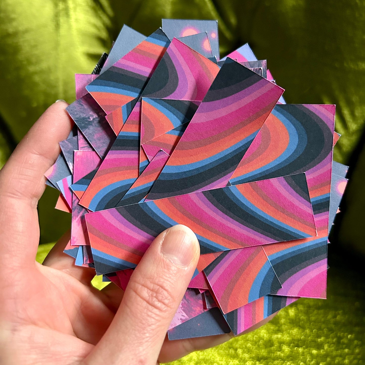 Hand holding a stack of colorful, patterned paper squares against a green fabric background