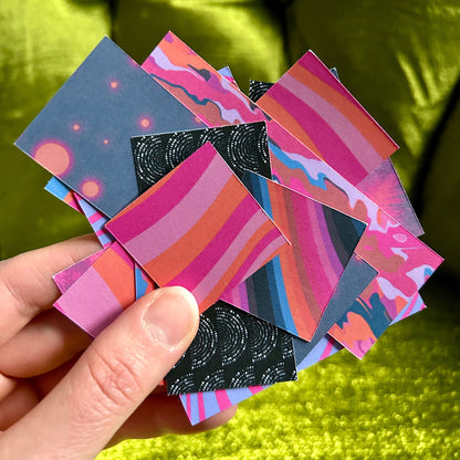 Hand holding a collection of colorful square sticker scraps with abstract designs against a green background