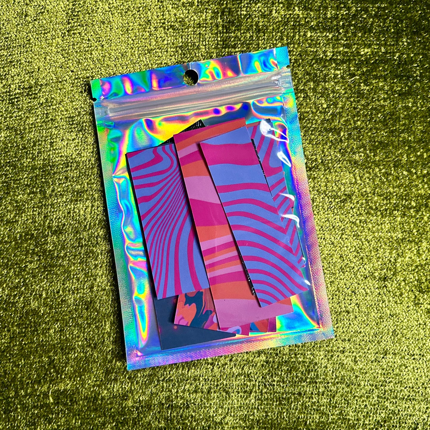 Holographic plastic bag with colorful sticker scraps on a green textured surface