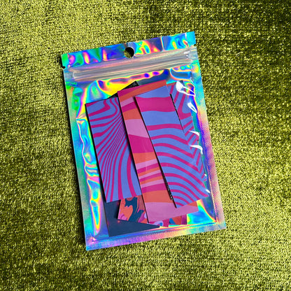 Holographic plastic bag with colorful sticker scraps on a green textured surface