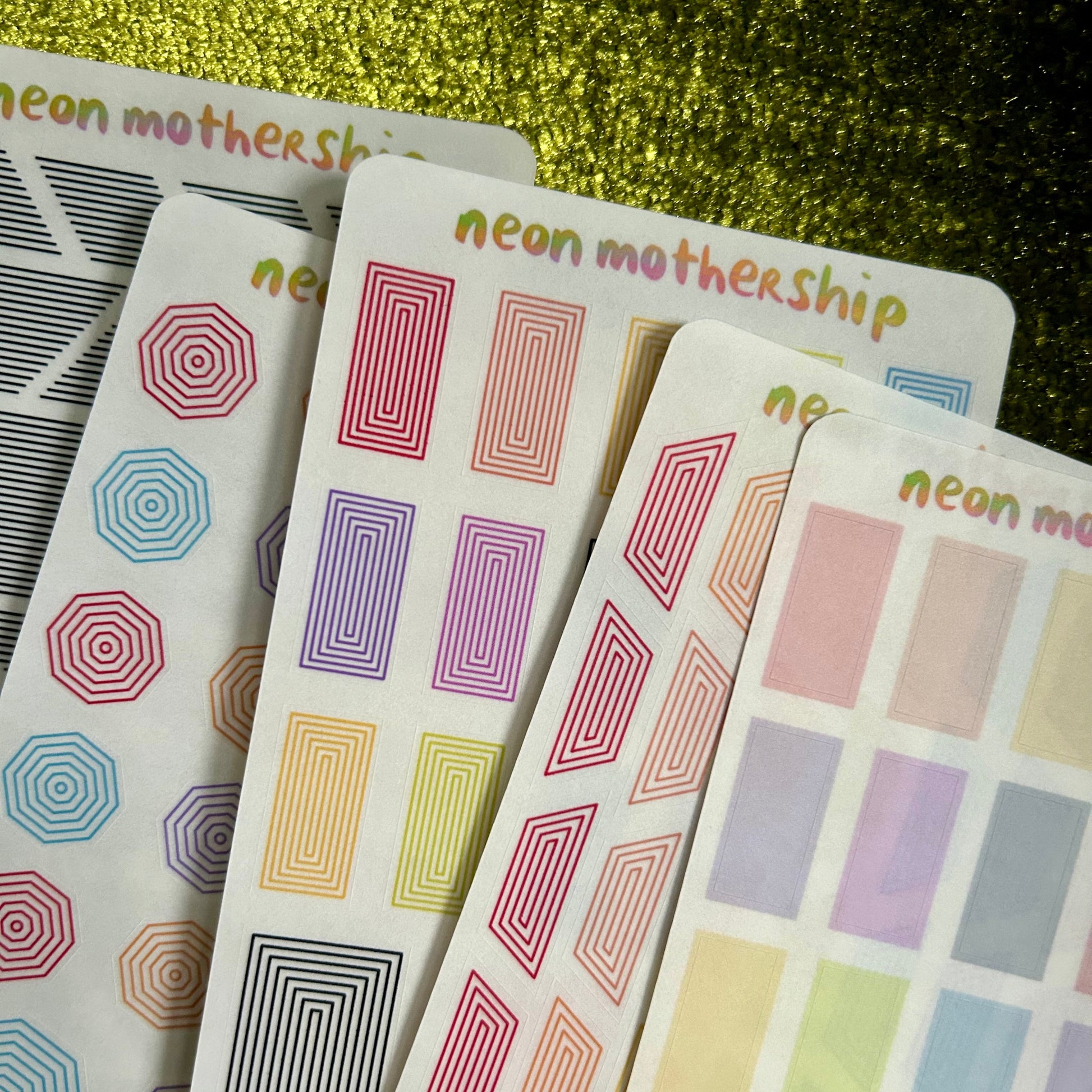 Set of colorful geometric patterned sticker sheets with 'neon mothership' branding on a glittery gold background.