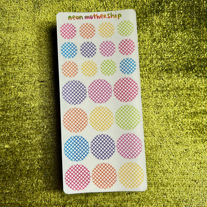 Sheet of colorful round stickers with grid patterns on a green textured surface