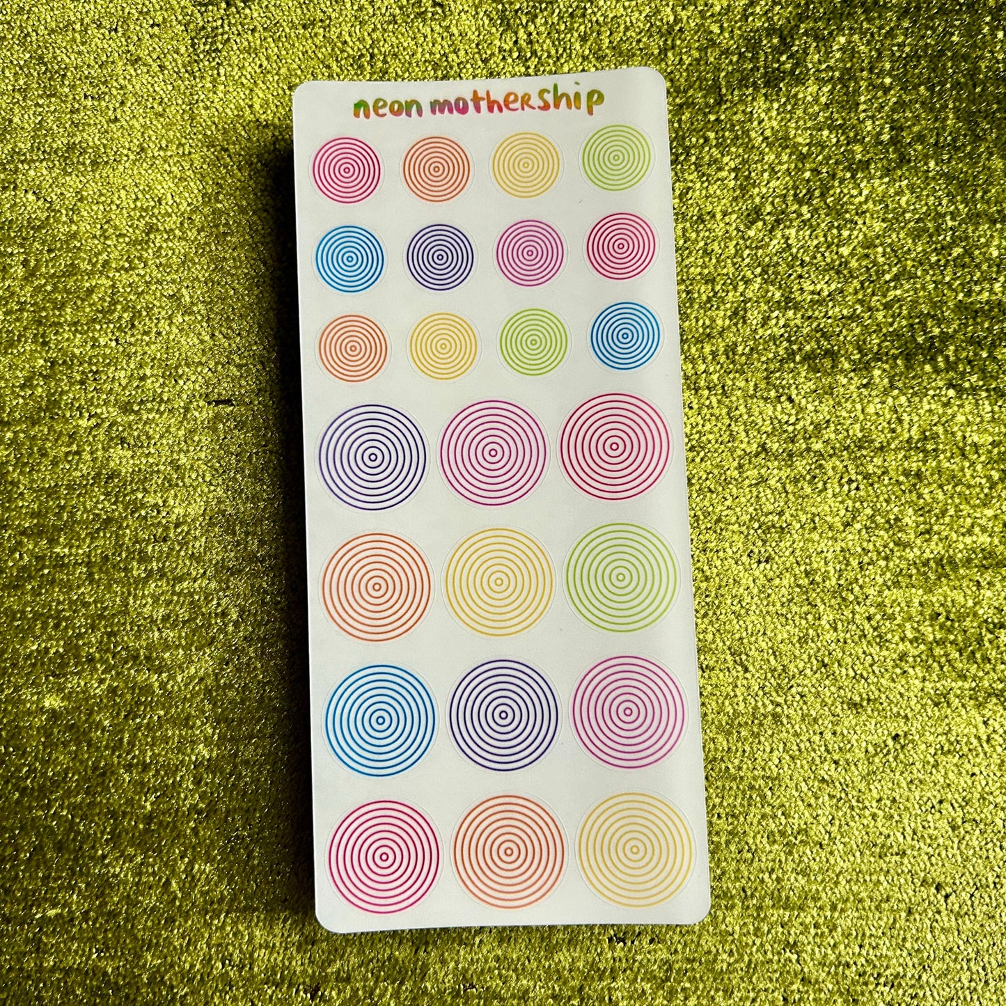Pack of colorful circular stickers on a green textured surface
