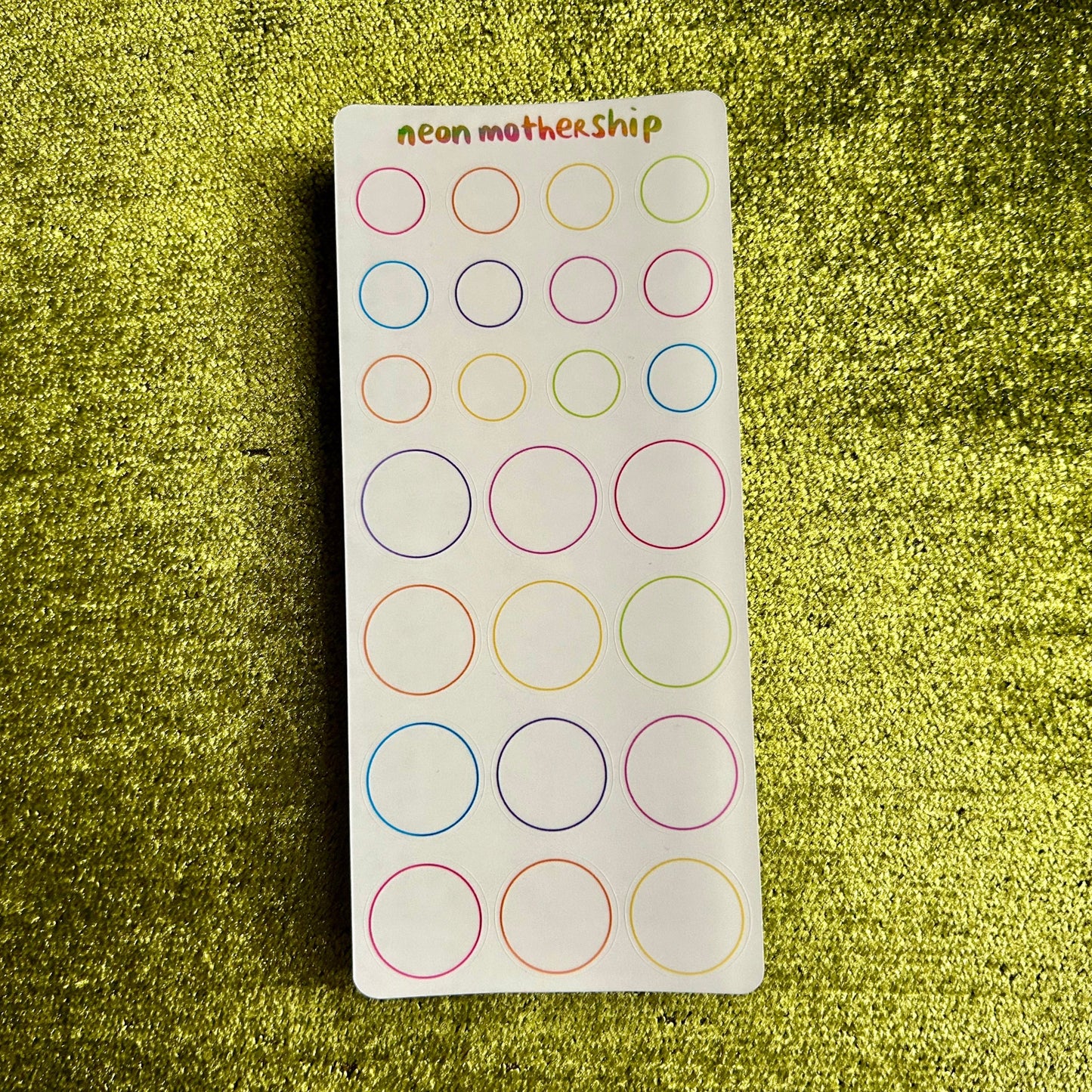 Sheet of circular stickers with colored borders on a green textured background