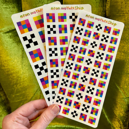 Three colorful sticker sheets held by a hand against a green fabric background