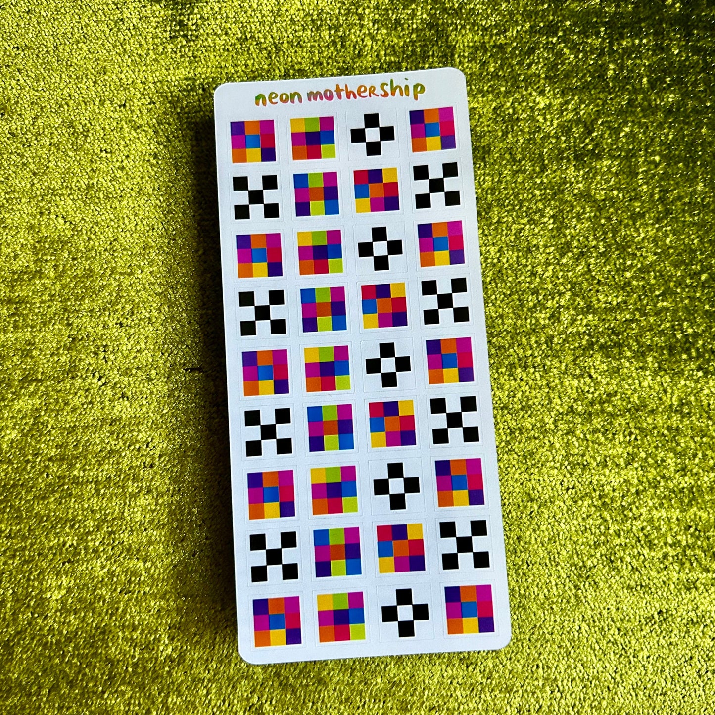 Sticker sheet with colorful square pattern stickers on a green textured surface