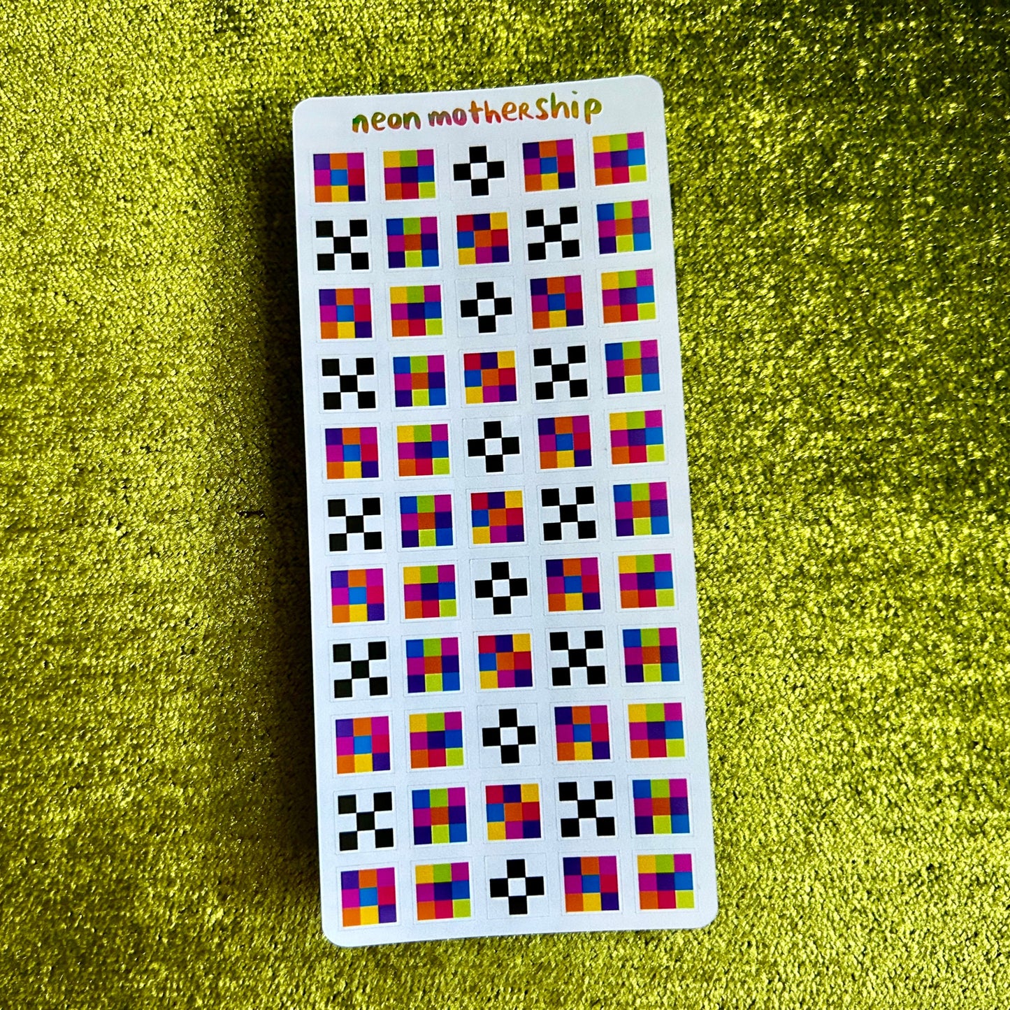 Sticker sheet with colorful square pattern on a green textured surface