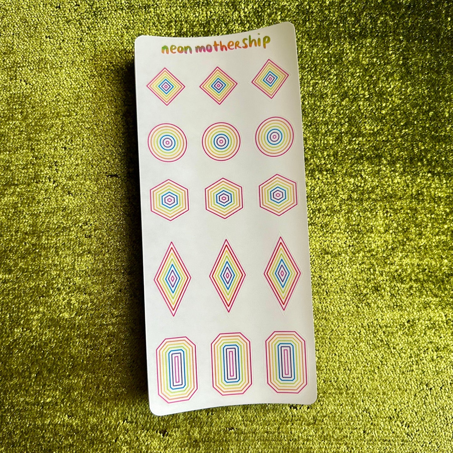 Sheet of colorful geometric stickers on a green textured surface