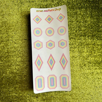 Sheet of colorful geometric stickers on a green textured surface