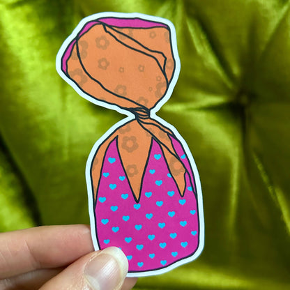 Sticker of a piece of spaceberry candy, held against a green fabric background.