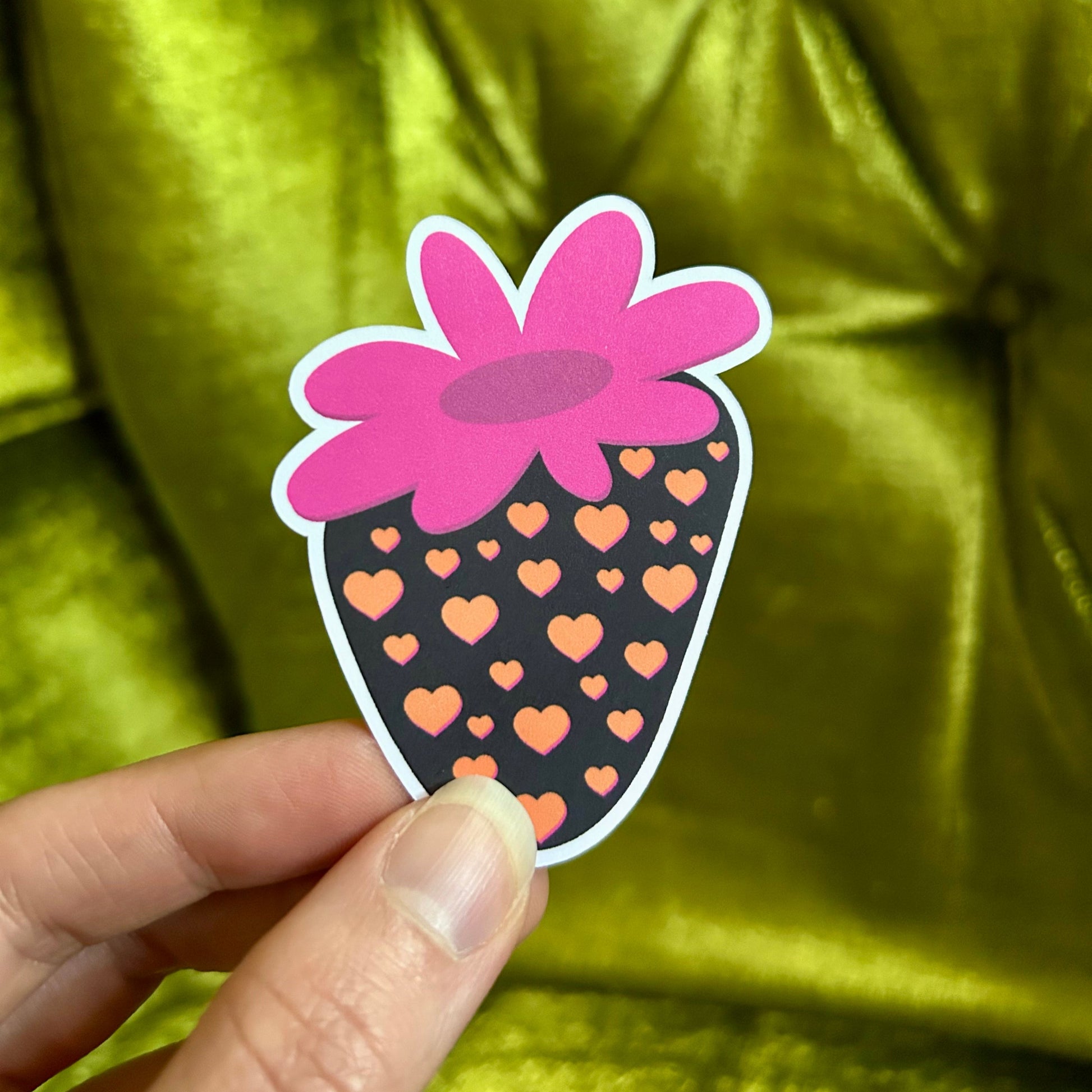 Sticker with pink flower design held by a hand against a green textured background