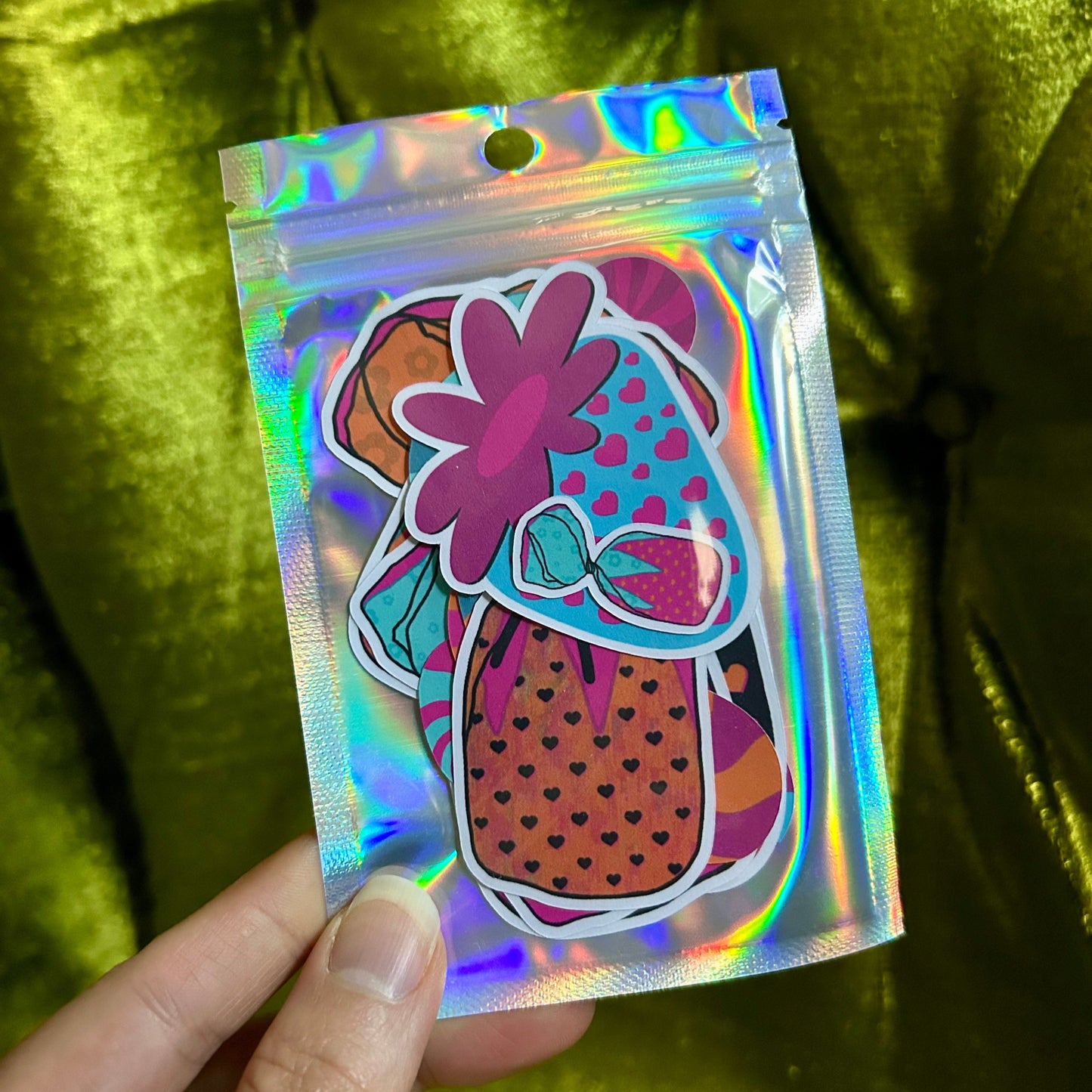 Holographic bag with a colorful design held by a hand against a green fabric background
