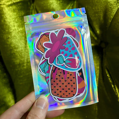 Holographic bag with a colorful design held by a hand against a green fabric background
