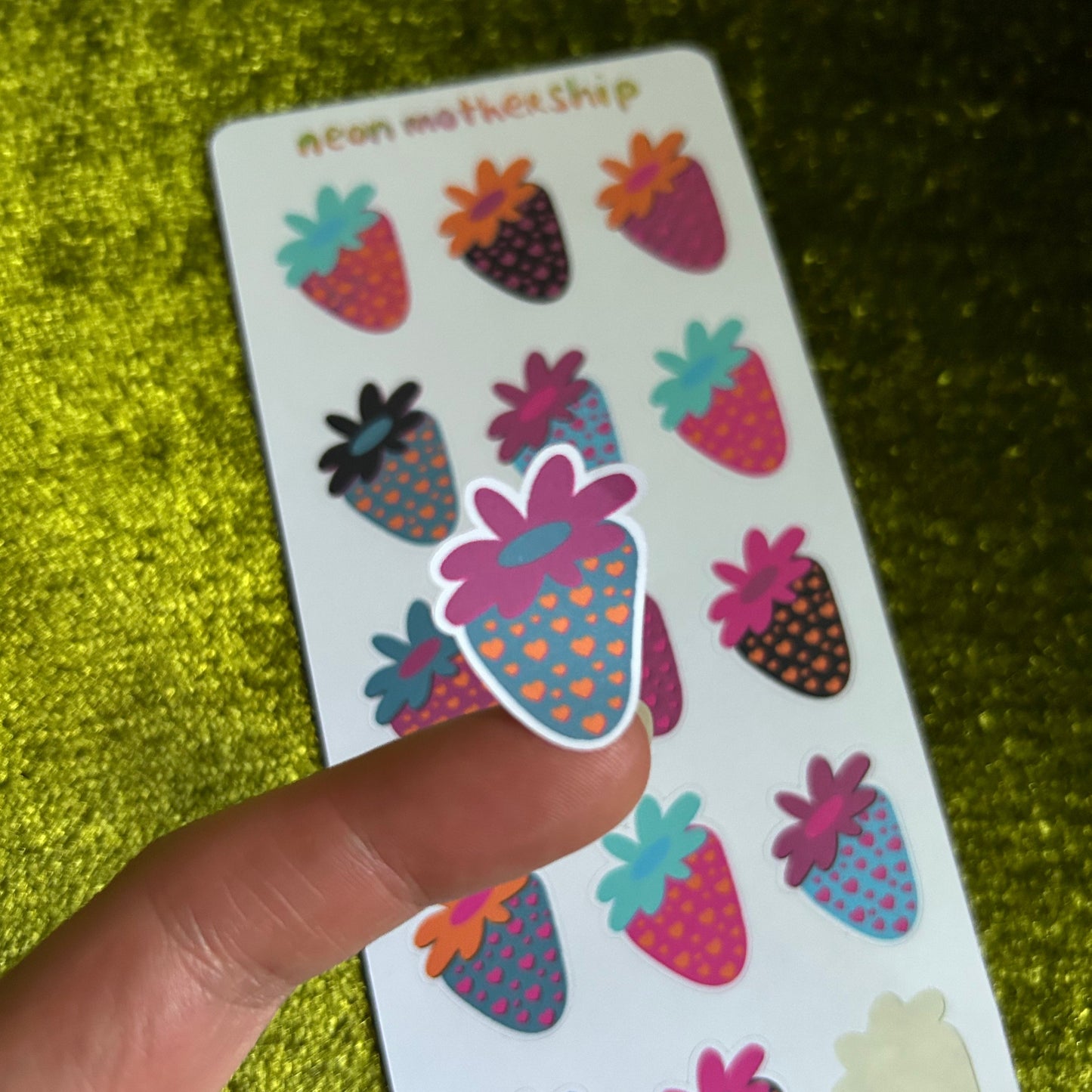 Colorful spaceberry stickers on a card held by a finger against a green textured background