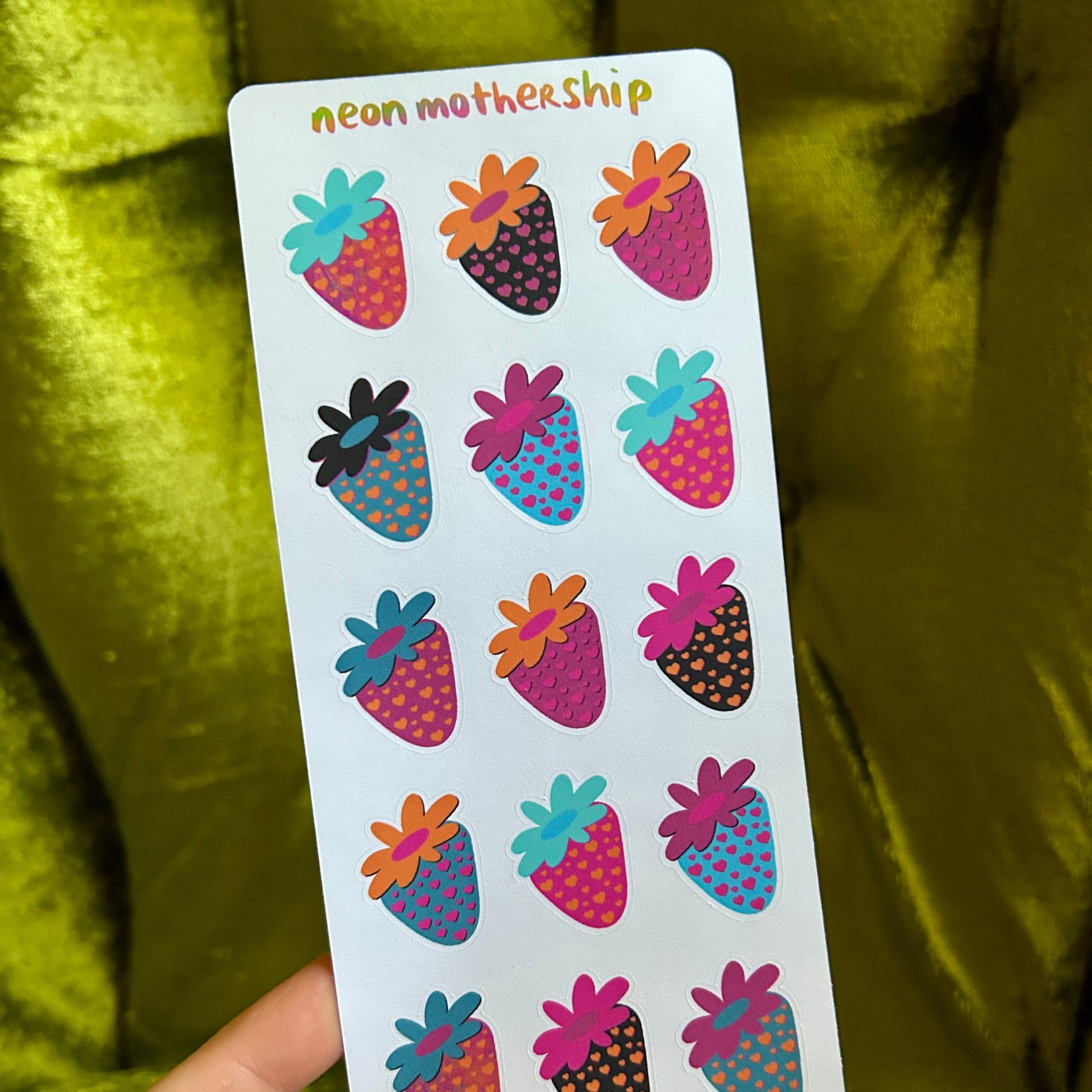 Sheet of colorful strawberry-shaped stickers held against a green fabric background