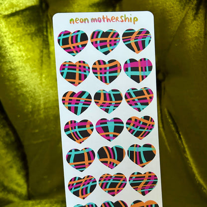 Sheet of colorful heart-shaped stickers held by a hand against a green fabric background