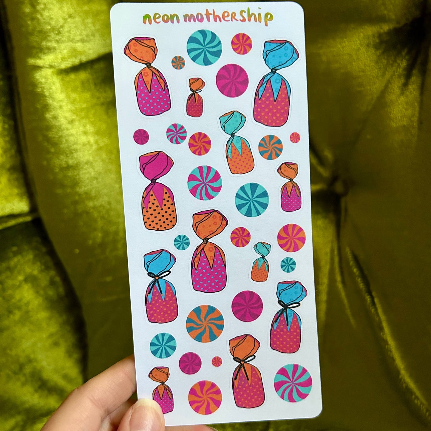 Sheet of colorful stickers held by a hand with a green fabric background