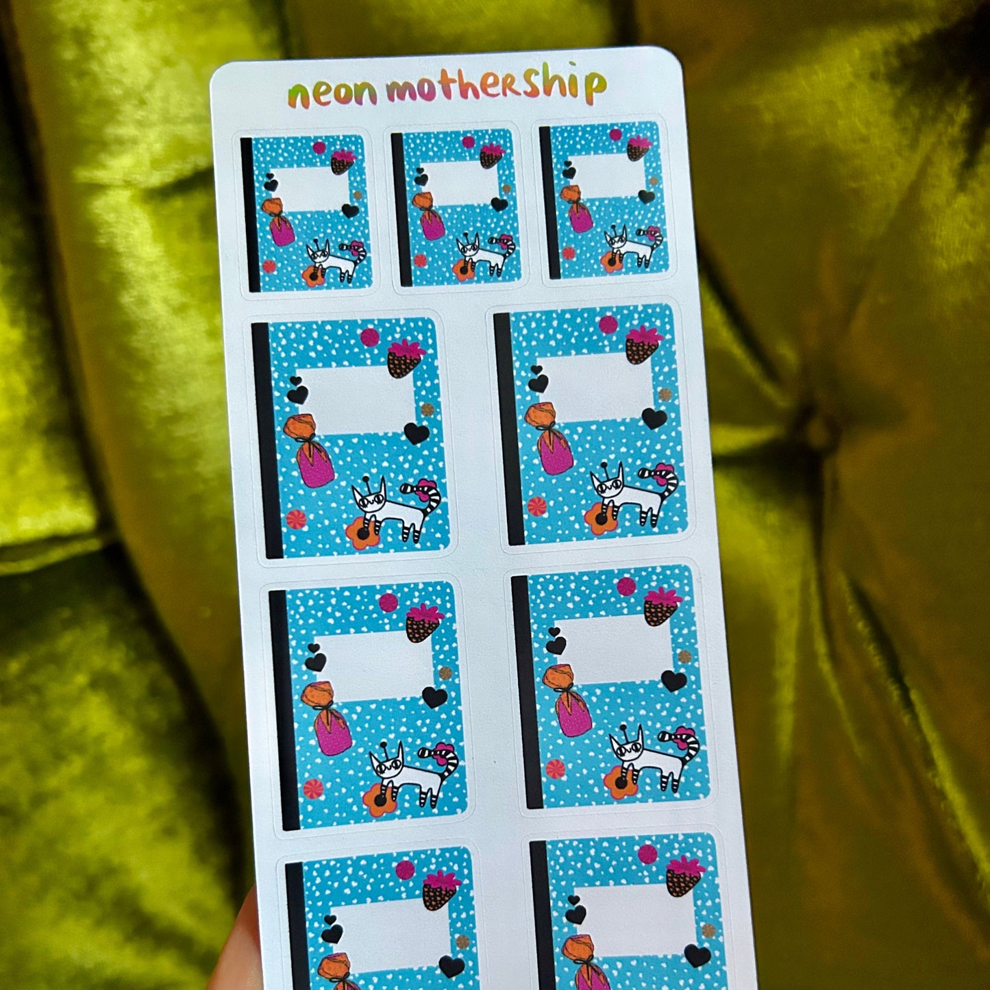 Sheet of stickers with cartoon designs held by a hand against a green fabric background