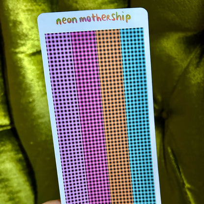 Card with colorful grid pattern held by a hand against a green fabric background