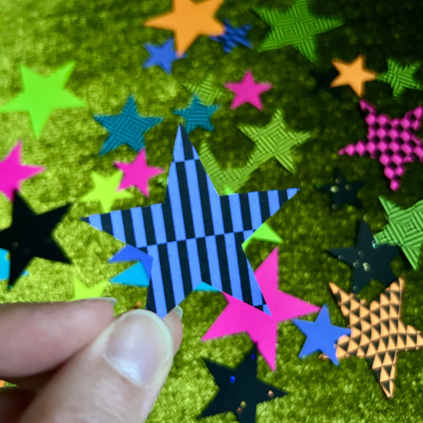 Colorful star-shaped papers on a green textured surface with a hand holding one of them.