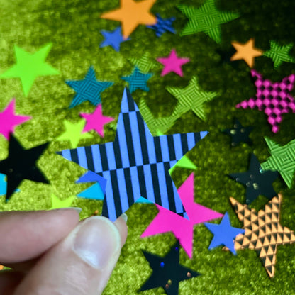 Colorful star-shaped papers on a green textured surface with a hand holding one of them.
