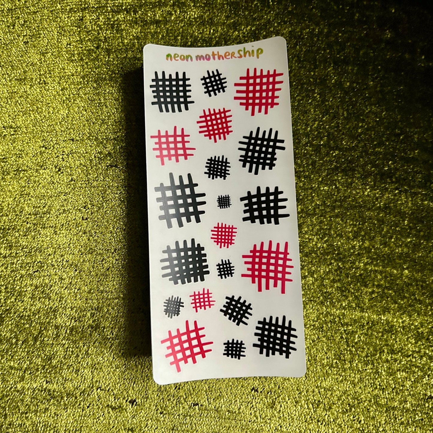 Sheet of stickers with black and pink designs on a green textured surface
