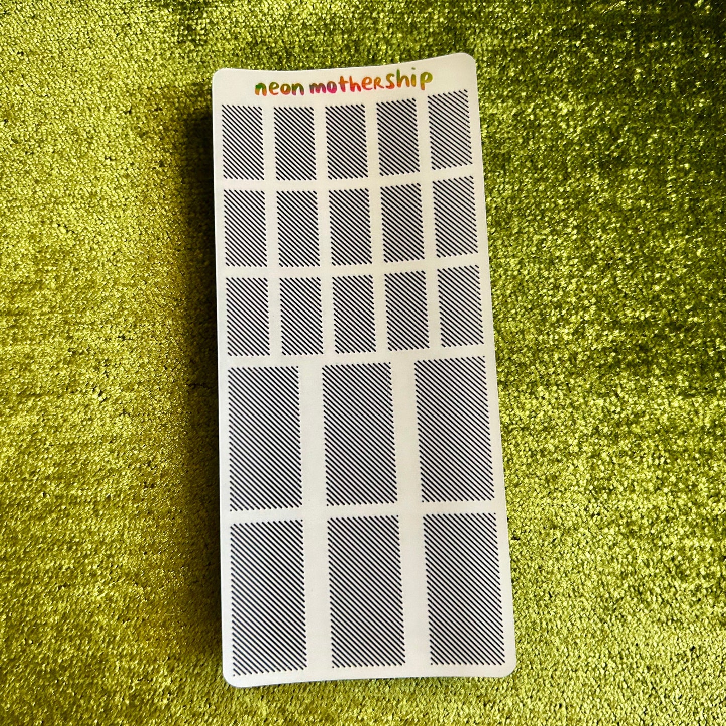 Small rectangular sticker sheet with 'neon motherShip' branding on a green textured surface