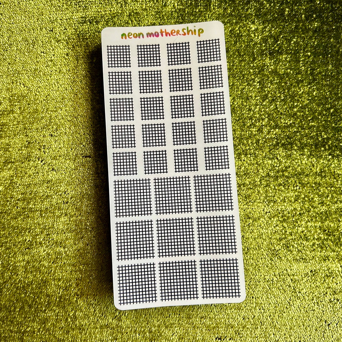 Grid-patterned sticker sheet on a green textured surface