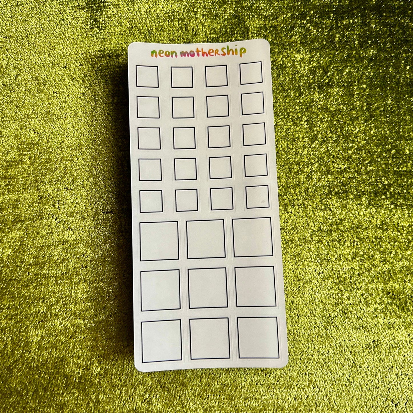 Rectangular sheet with square stickers on a green textured surface