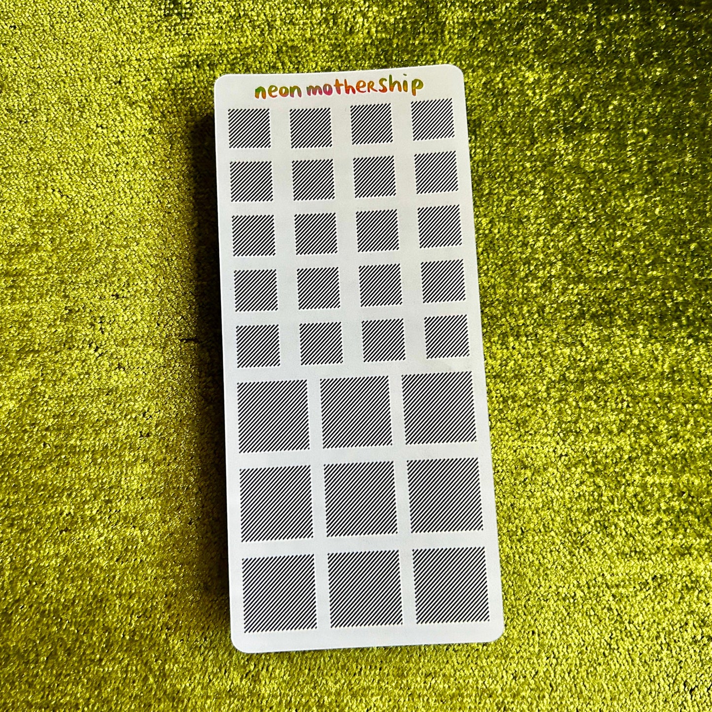 Rectangular sticker sheet with grid pattern on a green textured surface
