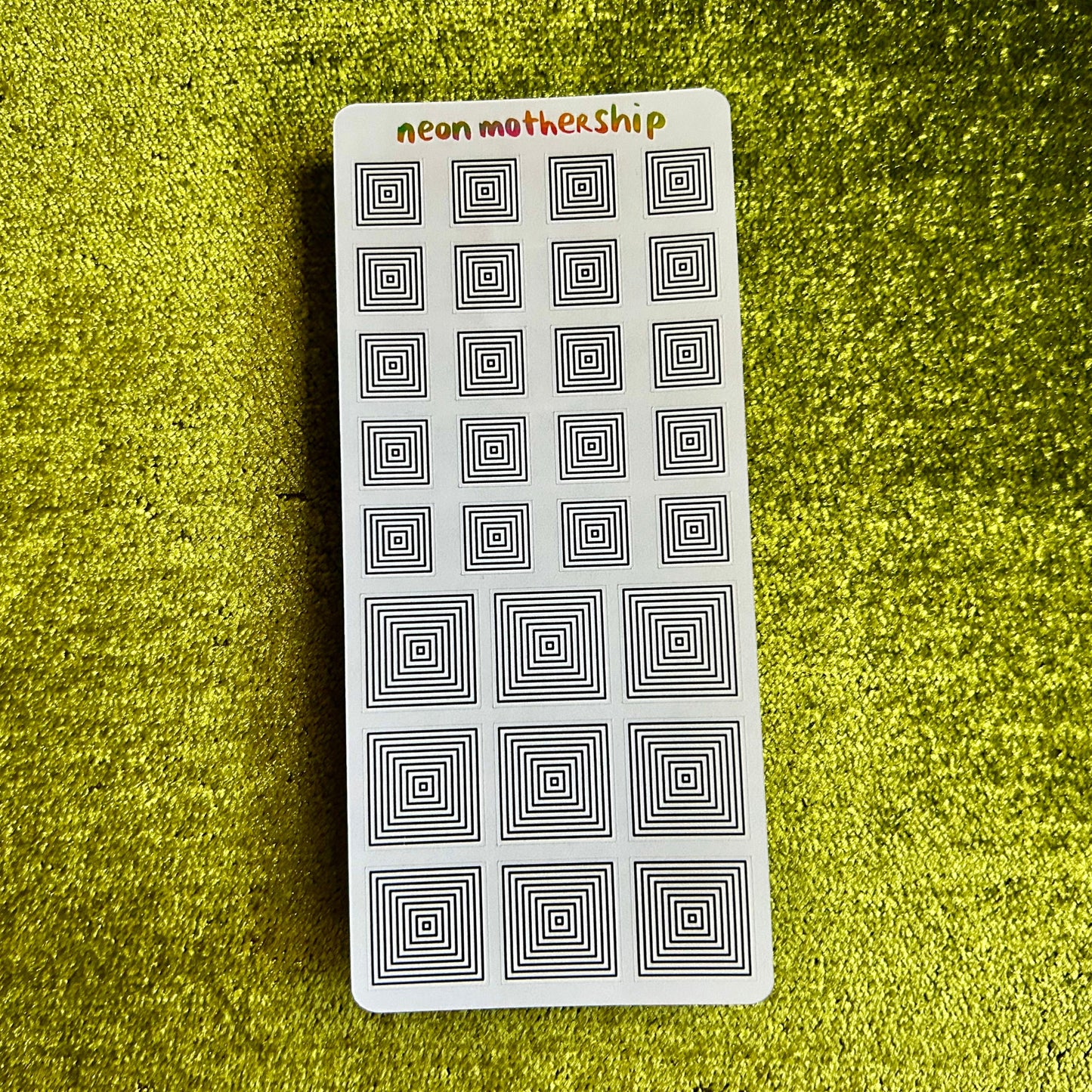 Rectangular sticker sheet with black square patterns on a green textured surface