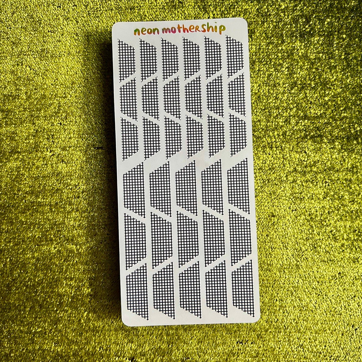 Rectangular white sticker sheet with black geometric pattern on a green textured surface