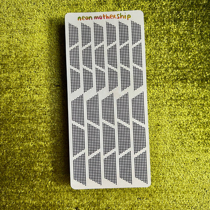 Rectangular white sticker sheet with black geometric pattern on a green textured surface