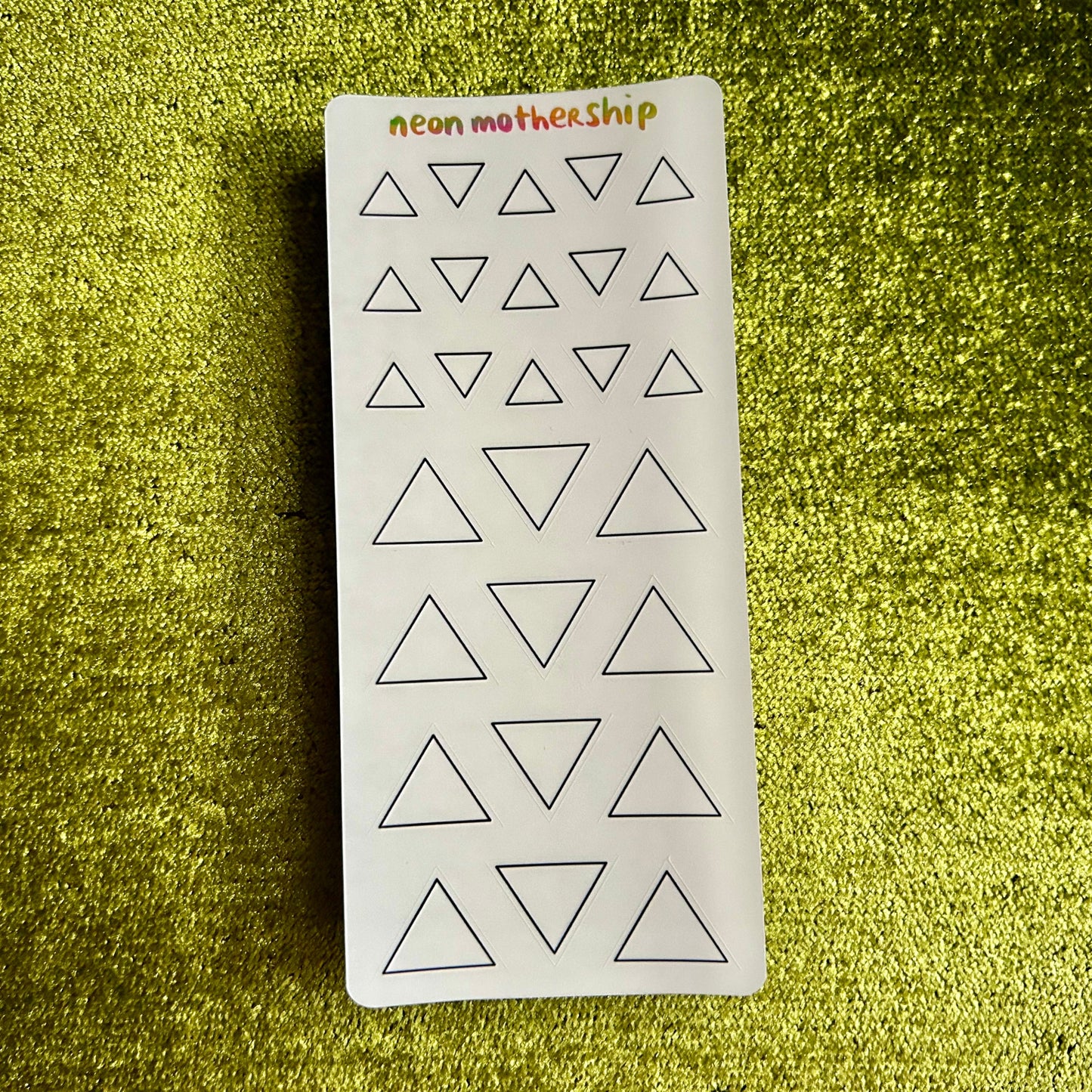 Sheet of triangle-shaped stickers with 'neon motherhip' branding on a green textured background