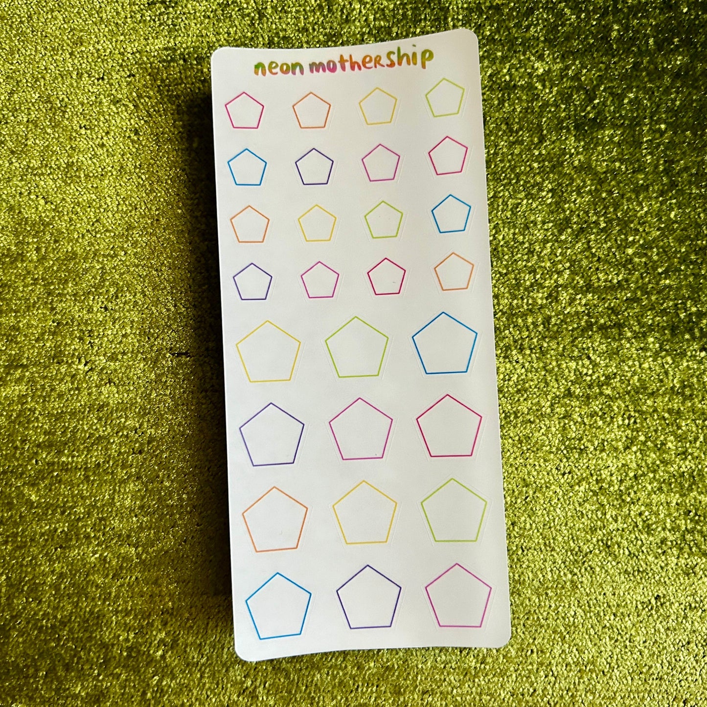 Sheet of colorful geometric stickers on a green textured surface