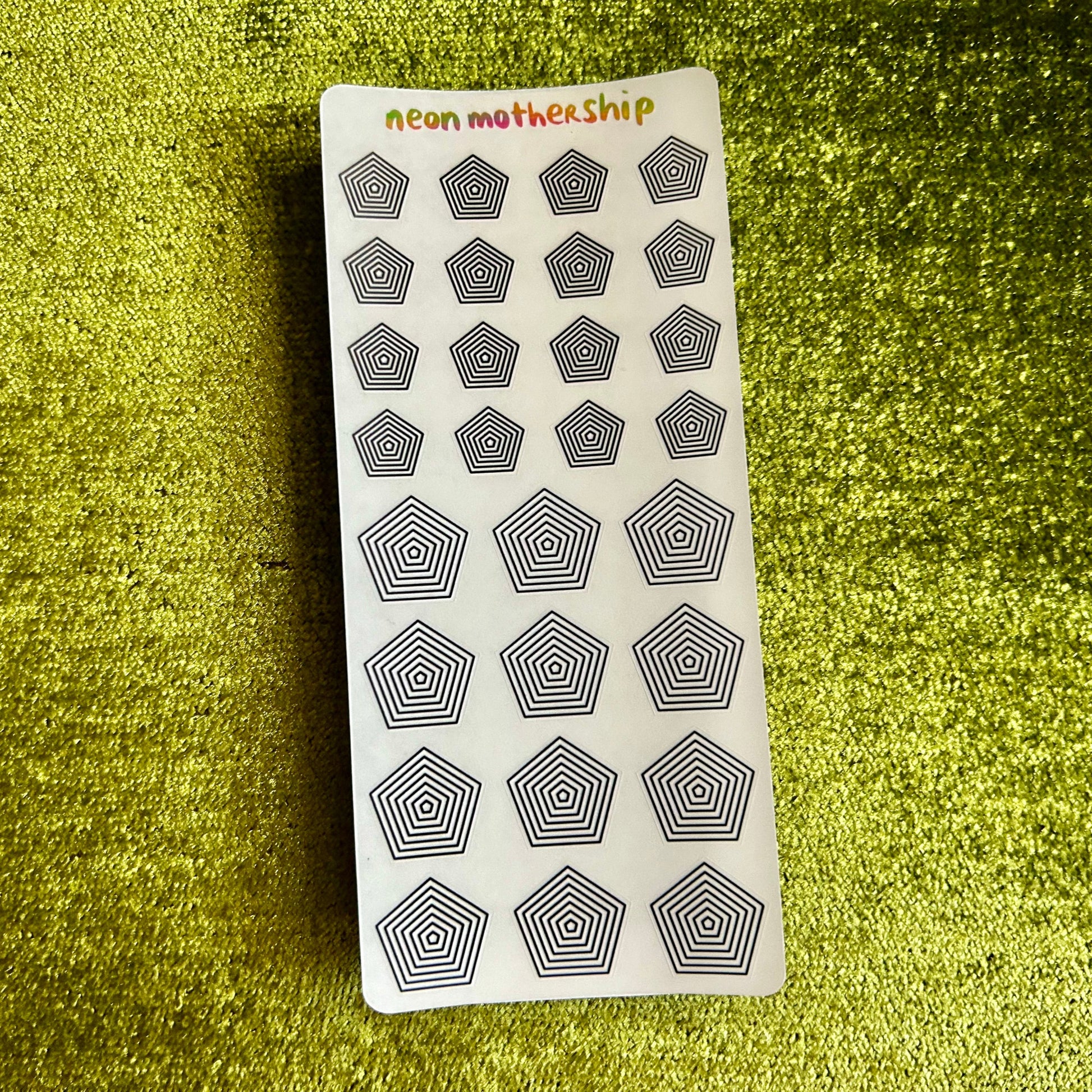 Sheet of geometric pentagon stickers with 'Neon Mothership' branding on a green textured background.