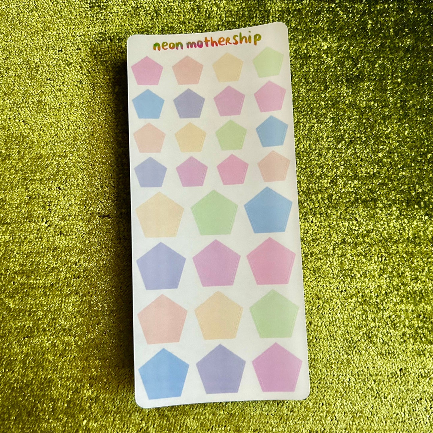 Sheet of colorful pentagon shaped stickers on a green glittery background