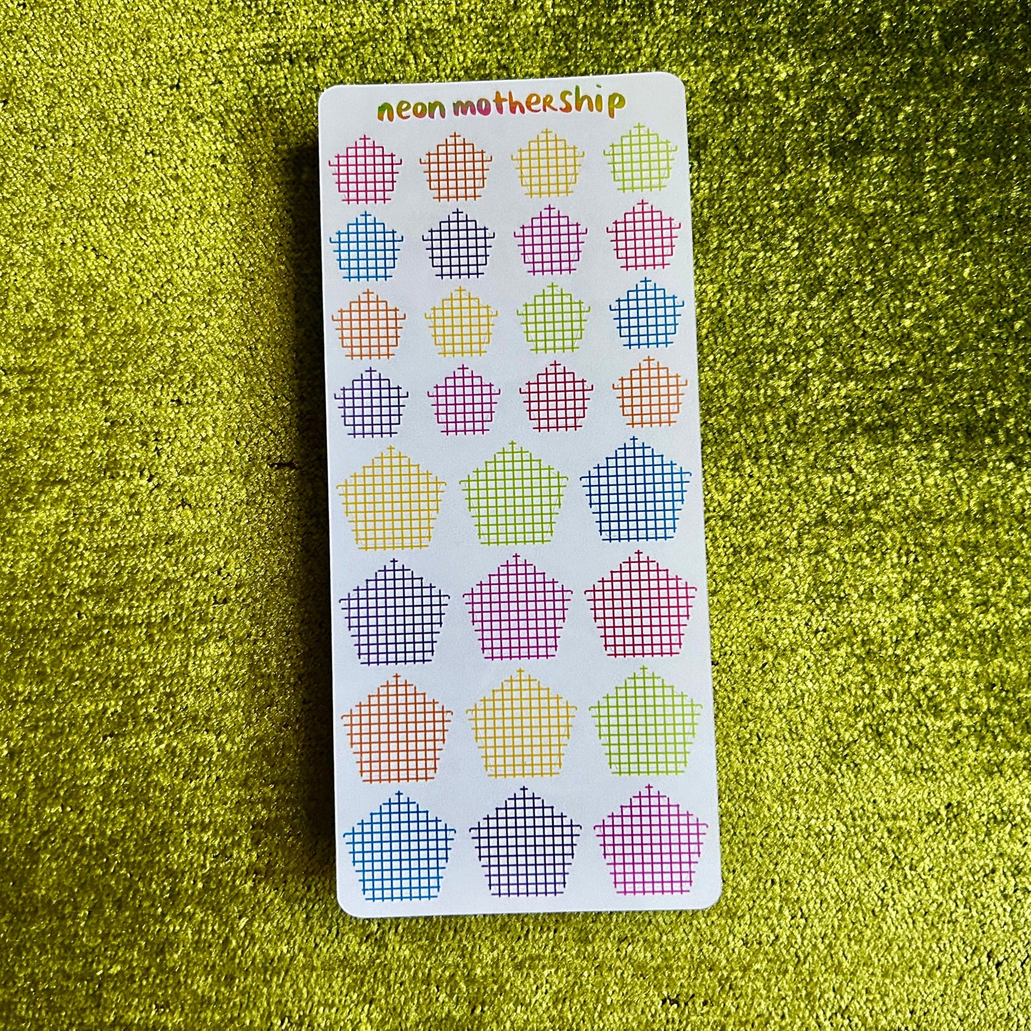 Sheet of colorful pentagon stickers on a green textured surface