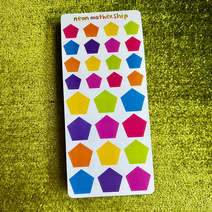 Colorful pentagon-shaped stickers on a white card with 'neon motherhip' branding, placed on a green textured surface.