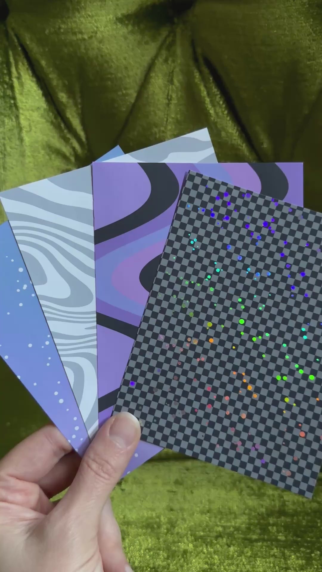a hand holds four patterned sticker sheets and waves the sheets back and forth to catch the light on holographic sparkles
