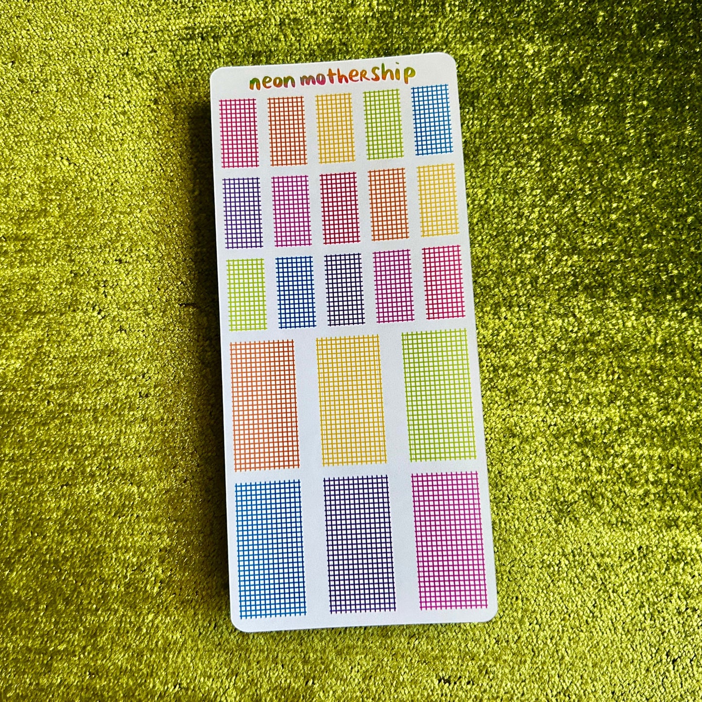Colorful grid patterned stickers on a green textured surface