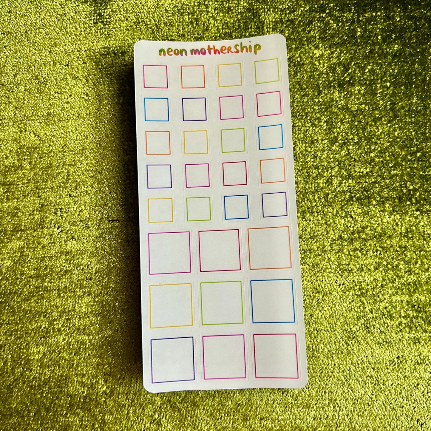 Sheet of colorful square stickers on a green textured background