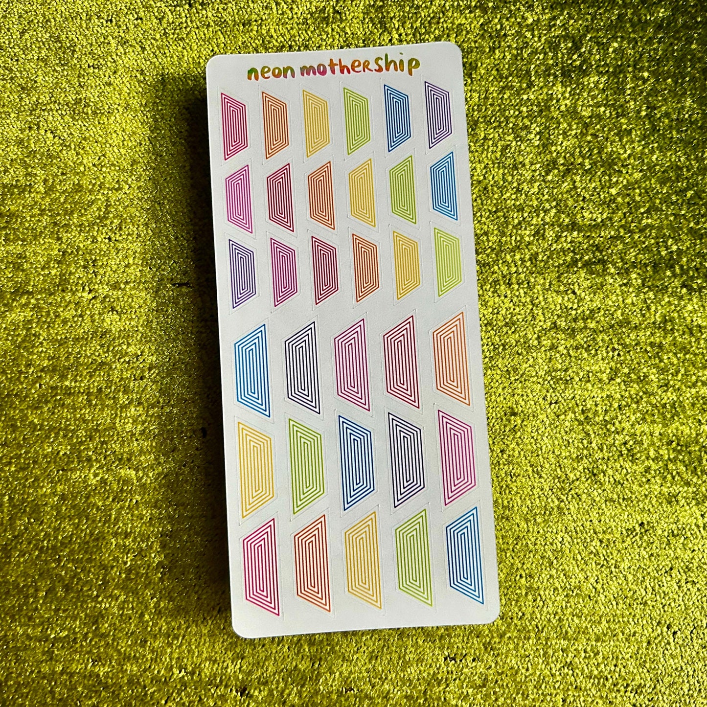 Sheet of colorful geometric stickers on a green textured surface