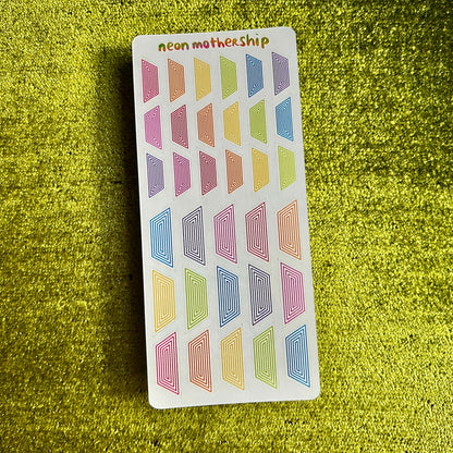 Sheet of colorful geometric stickers on a green textured surface